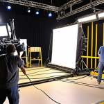 ** A bustling film set with crew members taping down cables and using cable ramps. The focus is on preventing tripping hazards. Include various film equipment like lights, cameras, and a dolly. The scene is brightly lit, emphasizing safety measures.

**